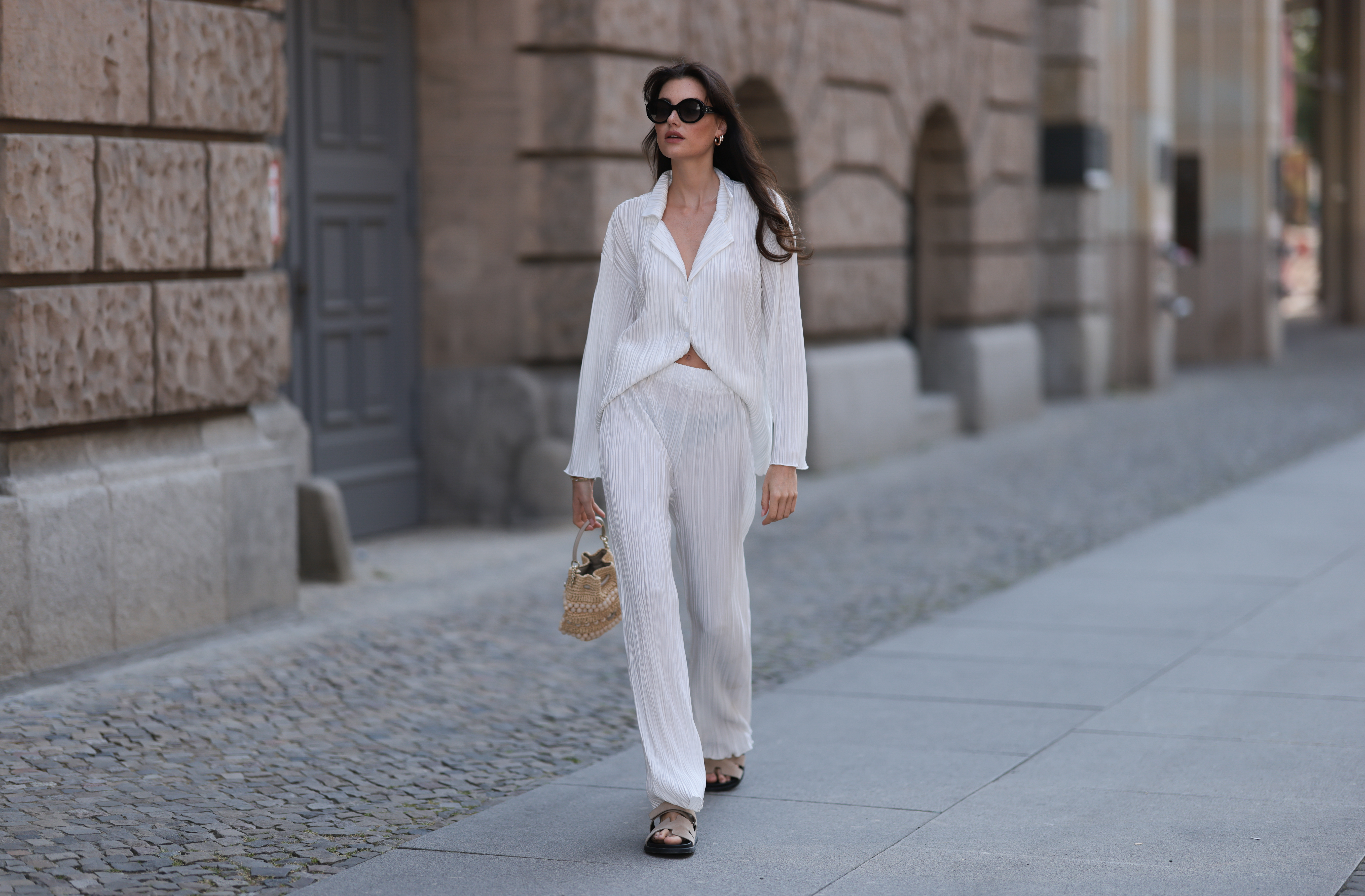 Celine Bethmann wears Hermes Chypre brown velvet leather sandals, Celine black shades, ninety9 matching white linen flannel and wide pants and Jimmy Choo mini raffia bast handbag on June 05, 2023 in Berlin, Germany.